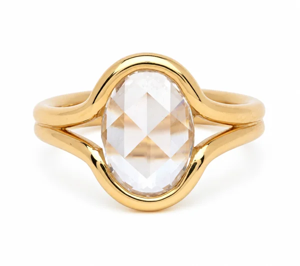 A faceted oval clear stone sits in a sculpted yellow gold ring with split, crossover shoulders.