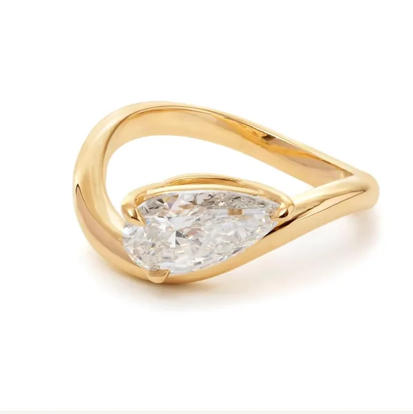 A pear-shaped clear stone sits in a polished yellow-gold ring.