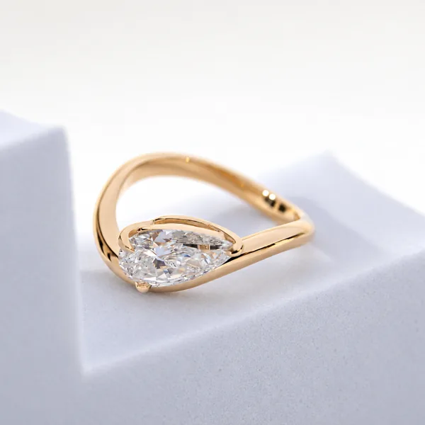 A pear-shaped clear stone sits in a yellow-gold ring with an open, curved band.