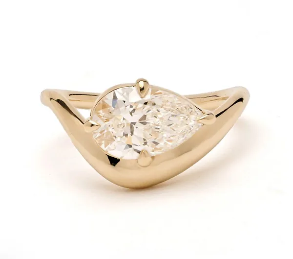 A large clear pear-shaped stone sits in a sculptural yellow-gold ring setting.
