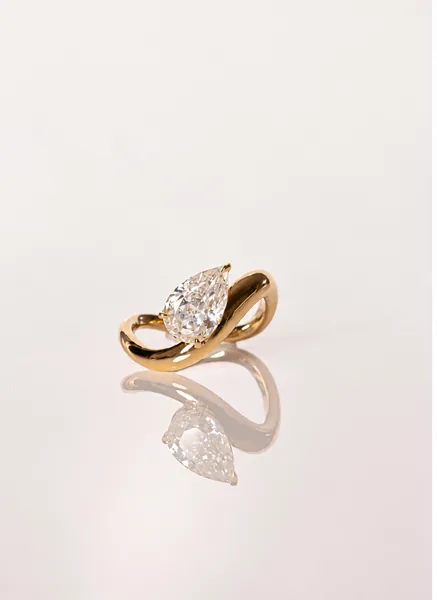 A pear-shaped clear stone sits in a polished yellow-gold ring with a looping band.