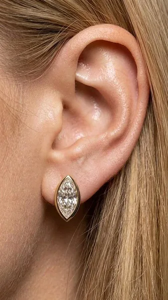 A marquise-shaped clear stone in a yellow-tone bezel setting hangs from the earlobe.