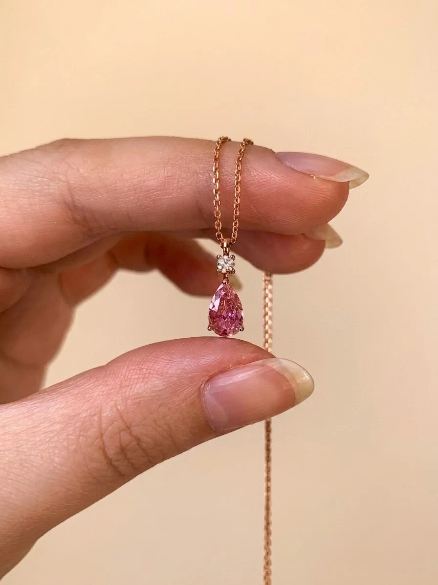 Pink pear drop necklace held between fingers