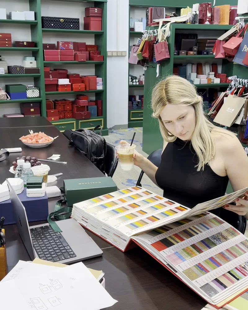 Ksenia Enbom looking through a book of material samples beside shelves of jewellery boxes