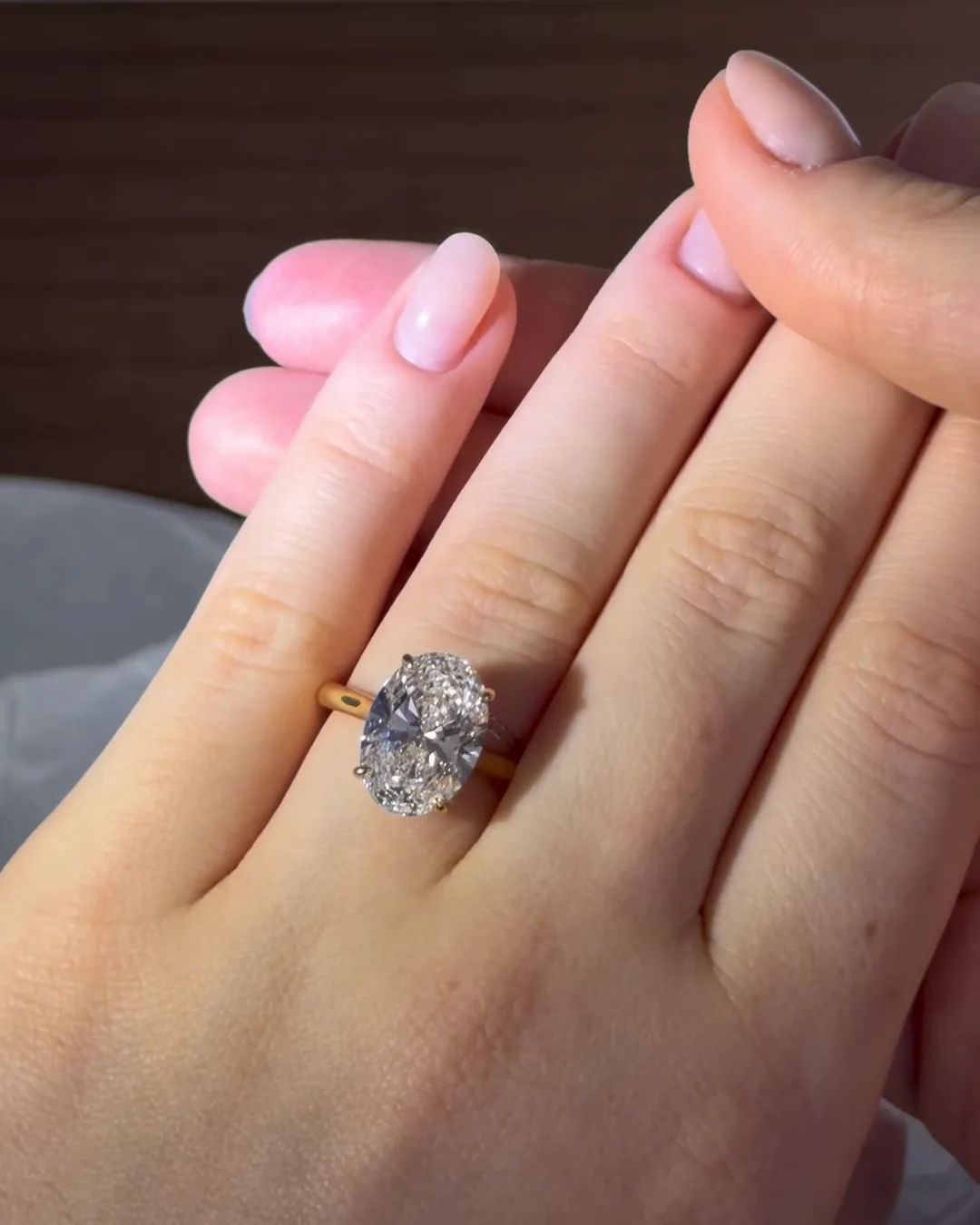A large oval white stone on a slim gold band, worn on a hand held against another