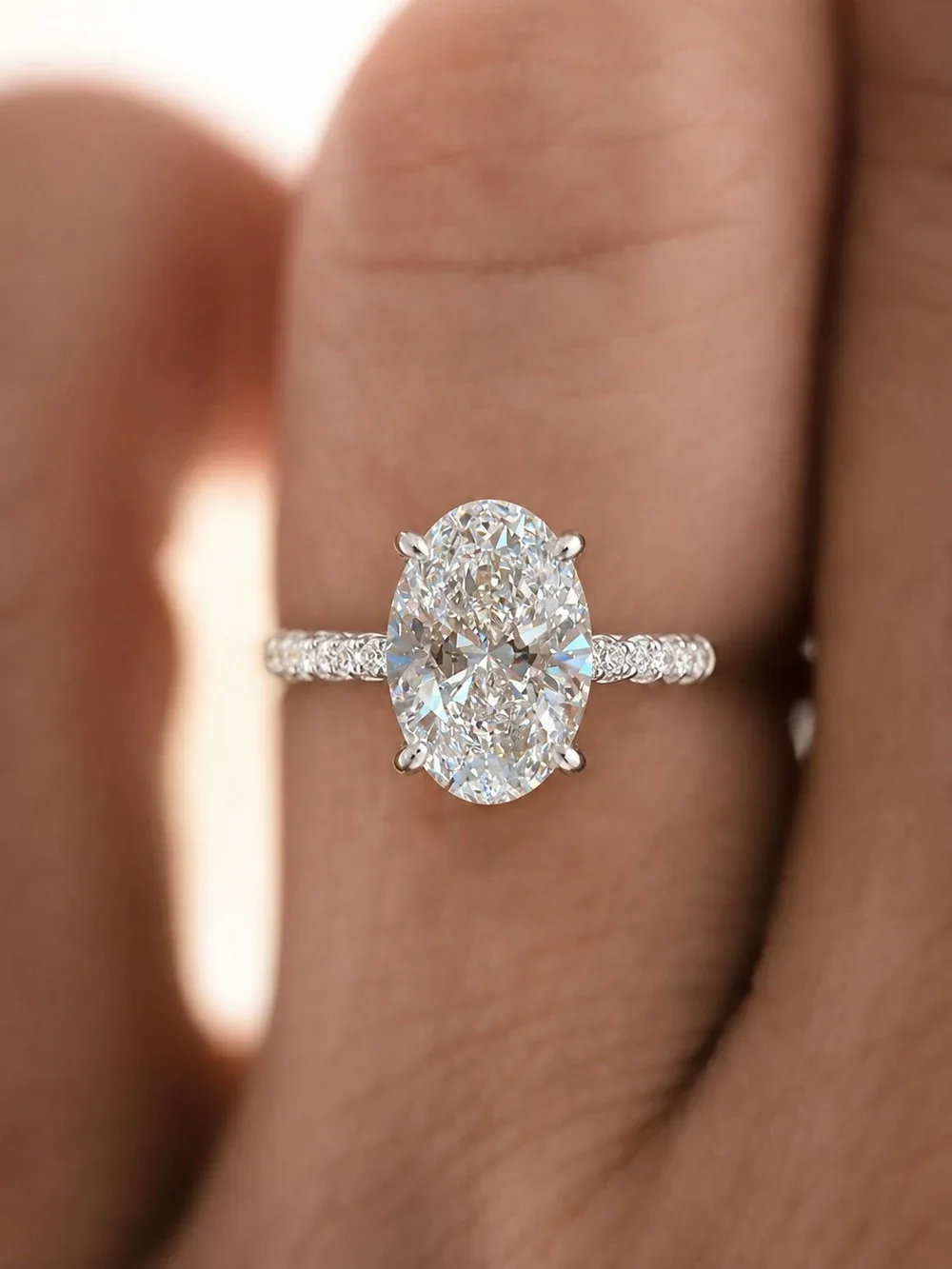 An oval white stone in four claws on a band set with small stones, seen from above on a finger