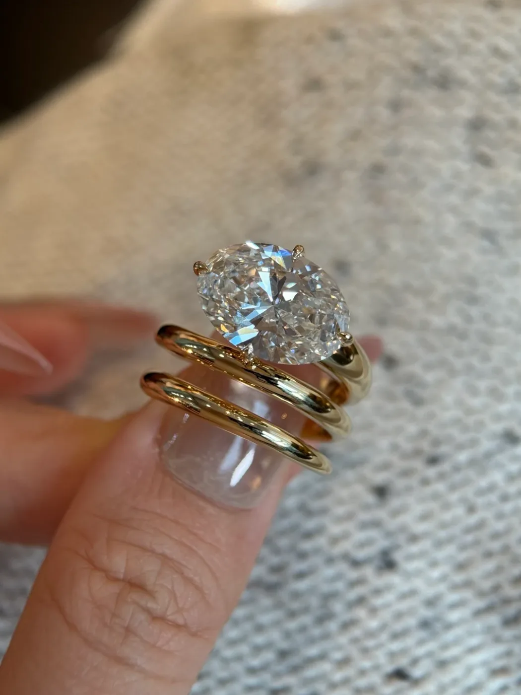 A pear-shaped white stone held on a fingertip beside two stacked gold bands.