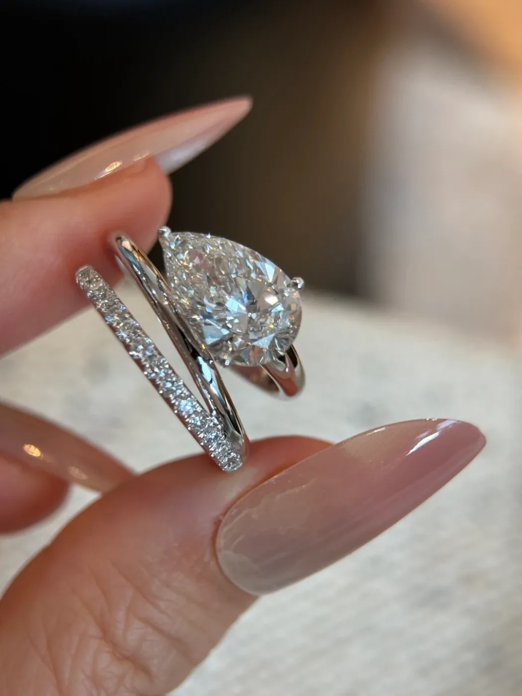 A pear-shaped white stone on a slim ring held beside a band set with small stones
