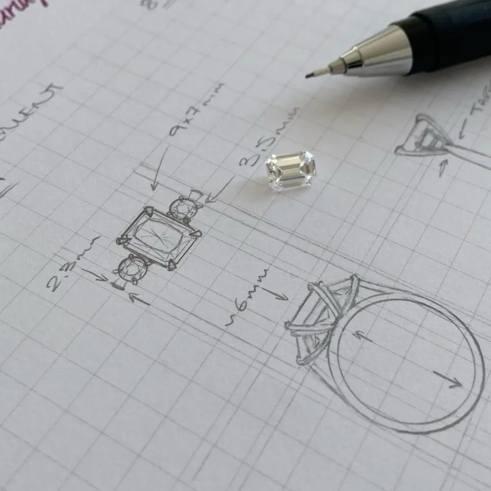 A loose emerald-cut stone on graph paper beside a pencil sketch of the ring it will be set in, measured in millimetres.